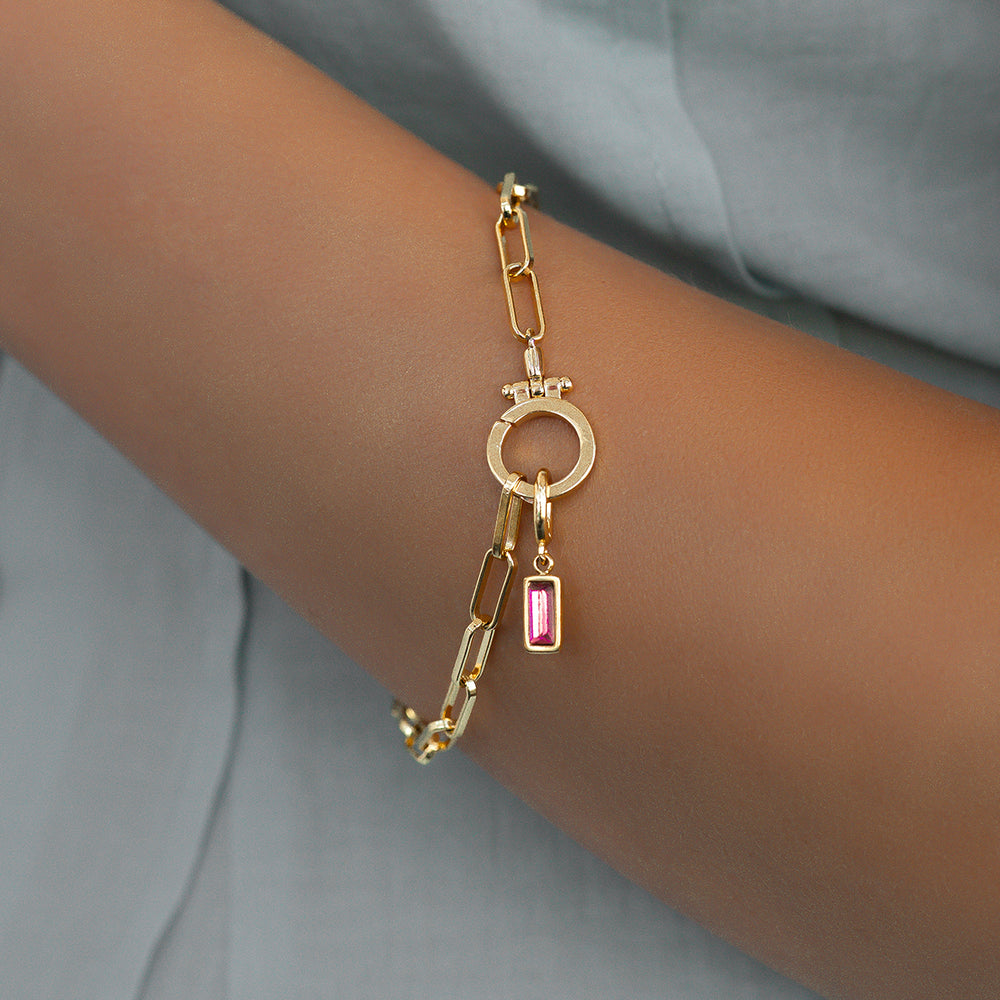 Gold bracelet with circular and rectangular charms on a wrist against a neutral background