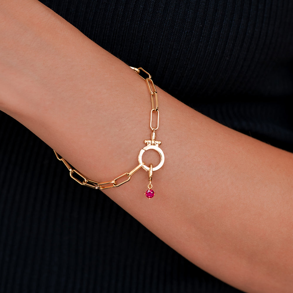 Gold bracelet with a pink gemstone on a wrist against a black background