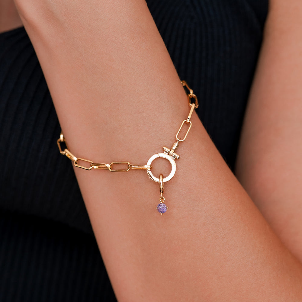 Gold bracelet with a purple gemstone on a wrist against a black background