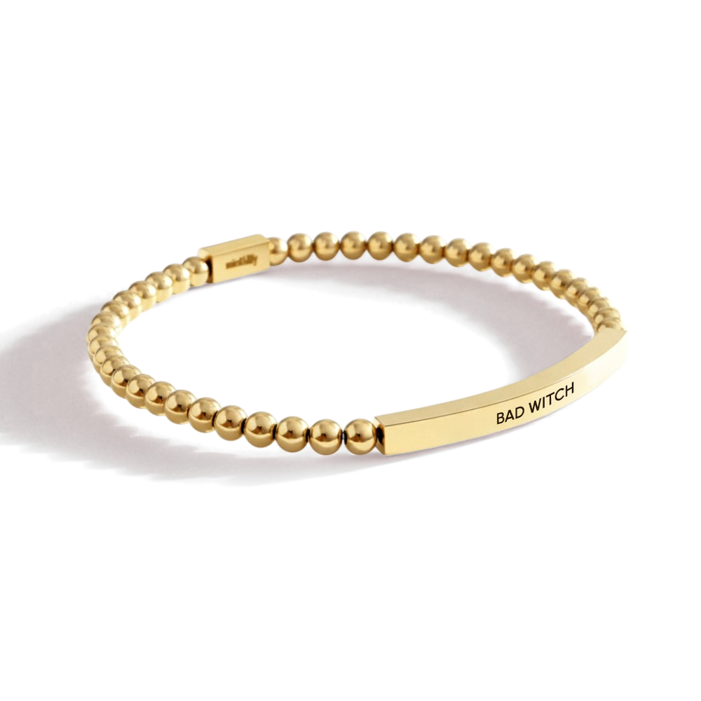 Gold beaded bracelet with 'BAD WITCH' tag on a white background