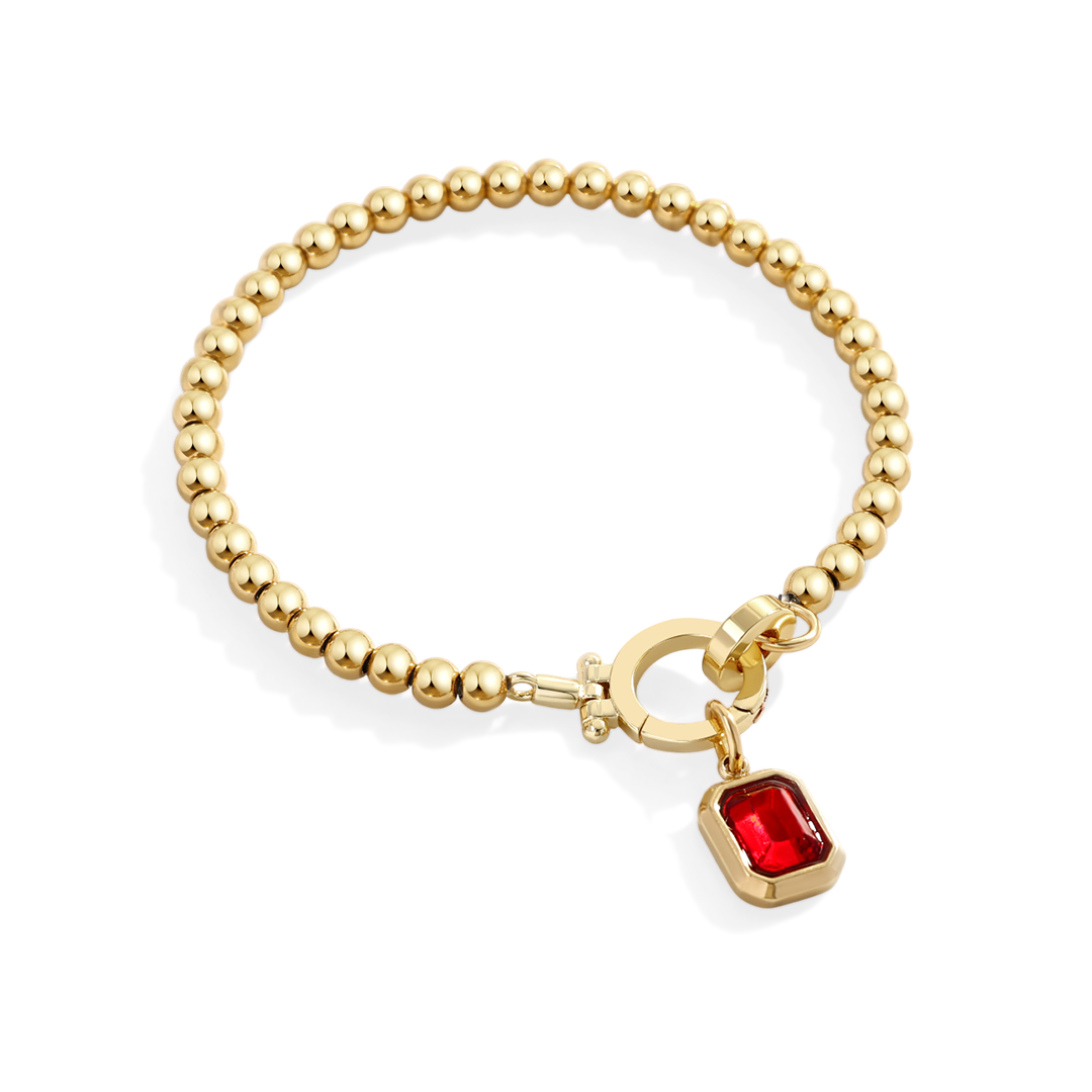 Gold bracelet with a red gemstone charm on a white background