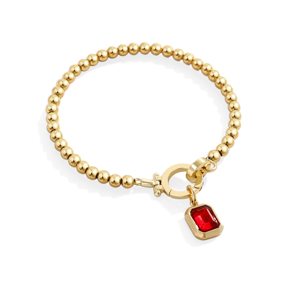 Gold bracelet with a red gemstone charm on a white background