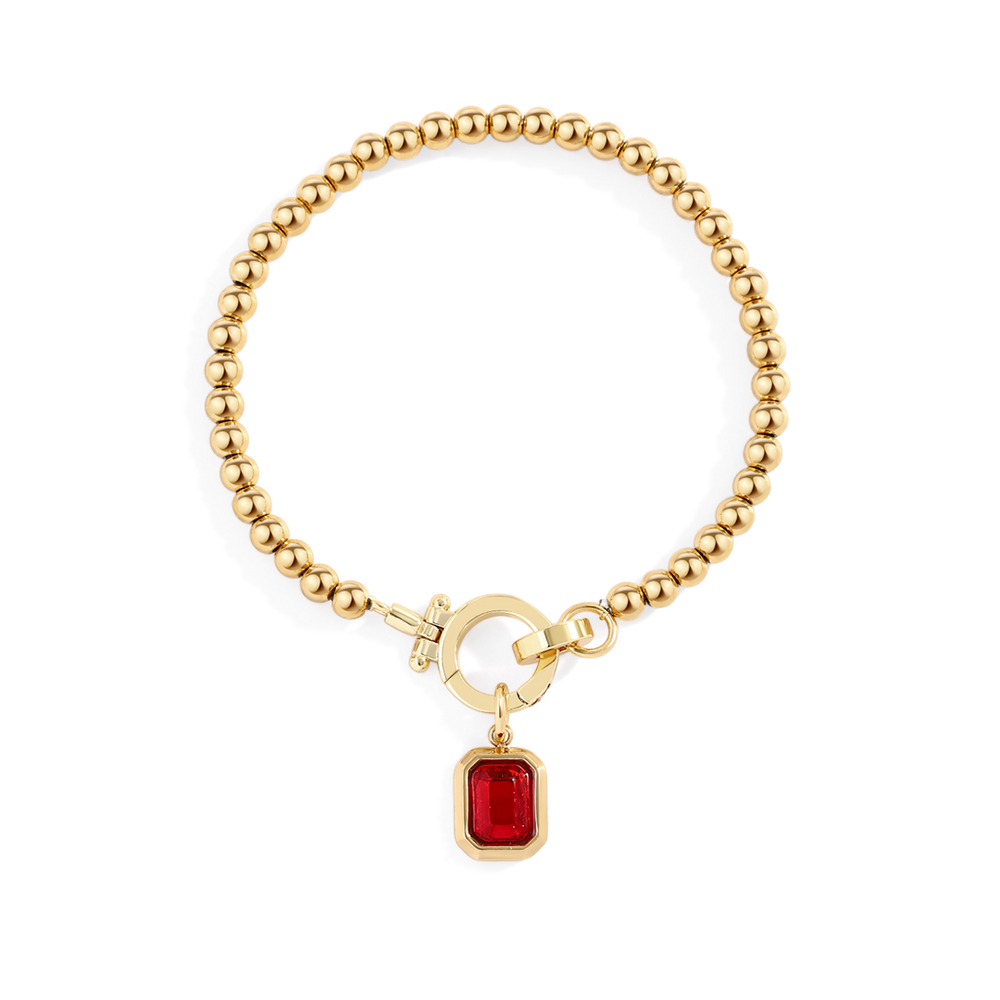 Gold bracelet with a red gemstone charm on a white background