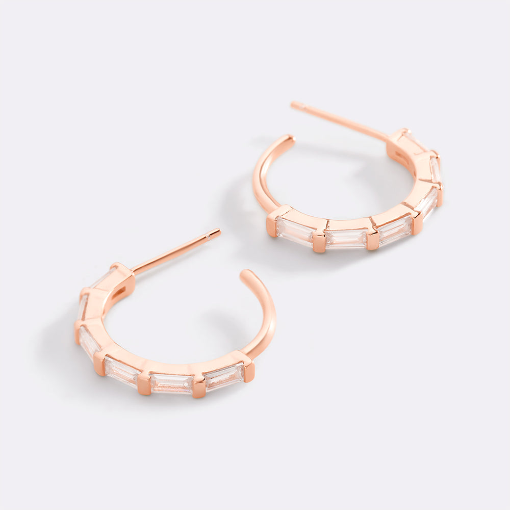 Rose gold hoop earrings with clear gemstones on a light gray background