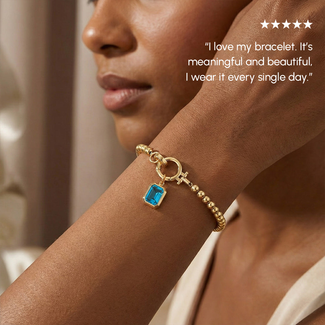 Woman wearing a gold bracelet with a blue gemstone, smiling.