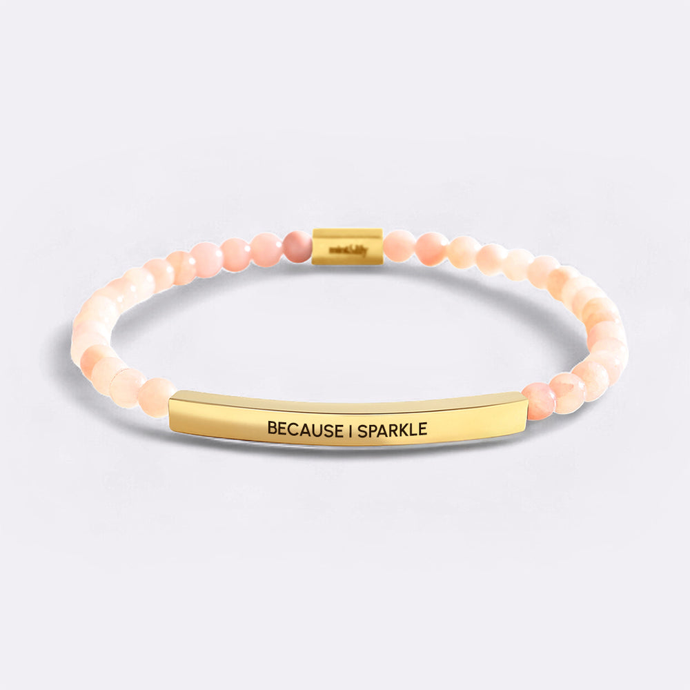 Bracelet with pink beads and gold bar with 'BECAUSE I SPARKLE' text on a light gray background