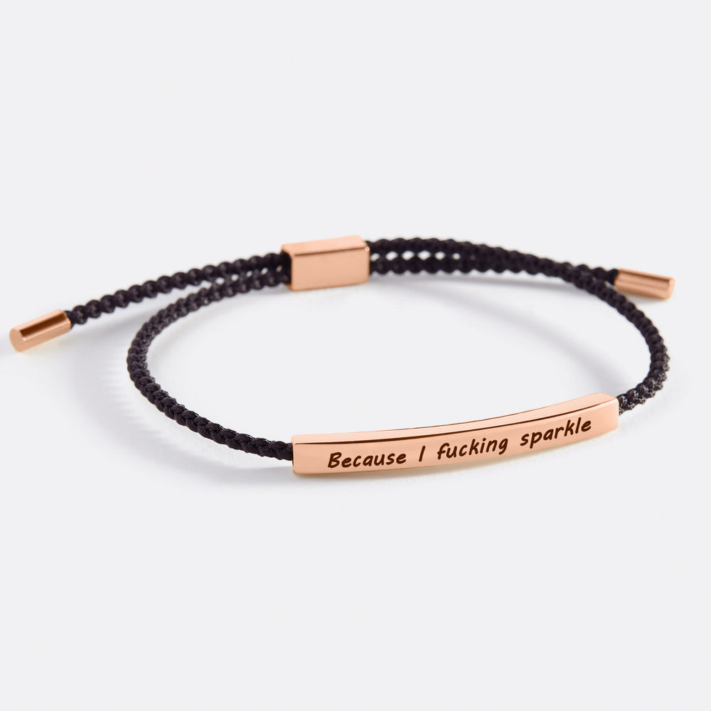 A braided bracelet with gold plating and a text charm that reads 'because i fucking sparkle'