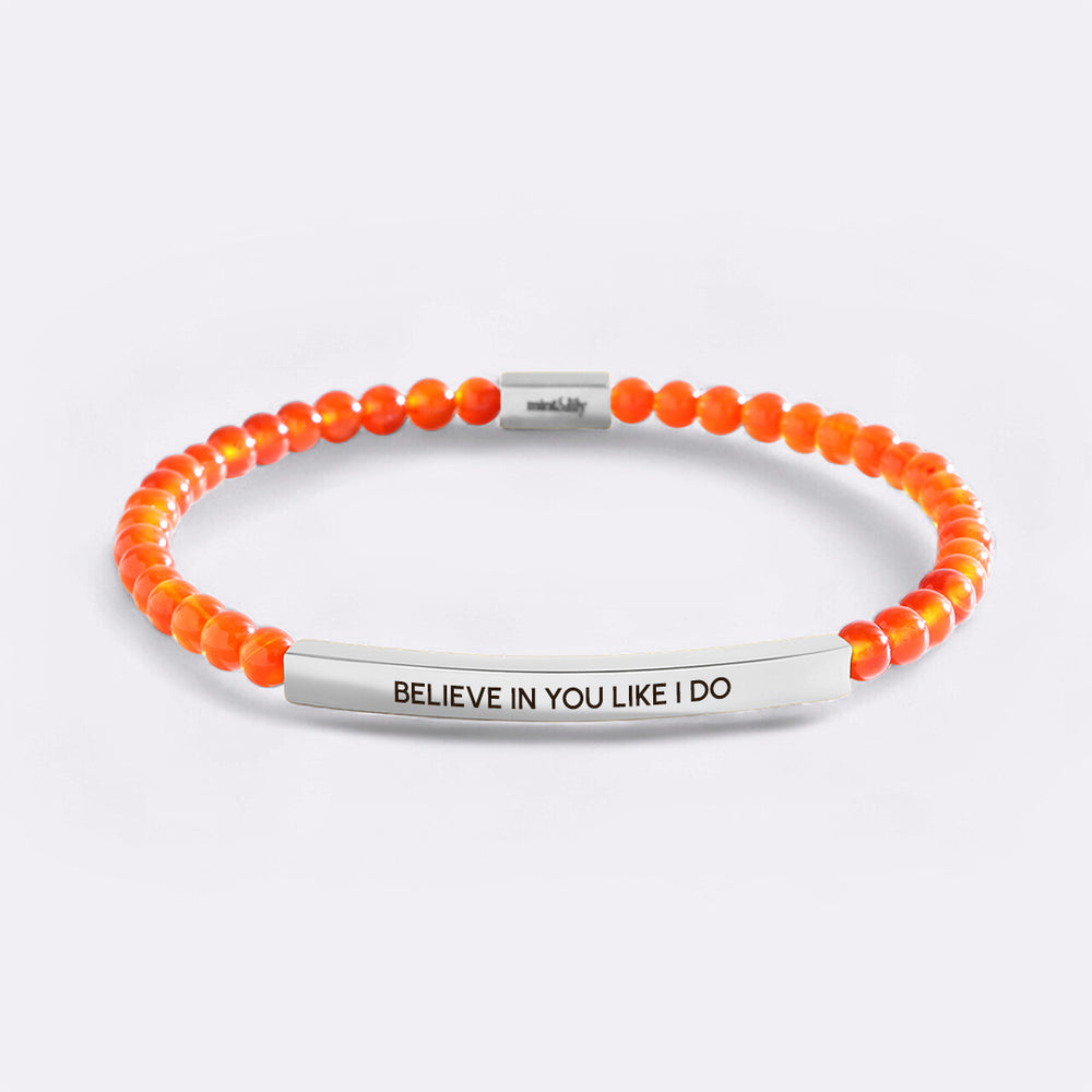 Bracelet with orange beads and silver bar engraving on a light gray background