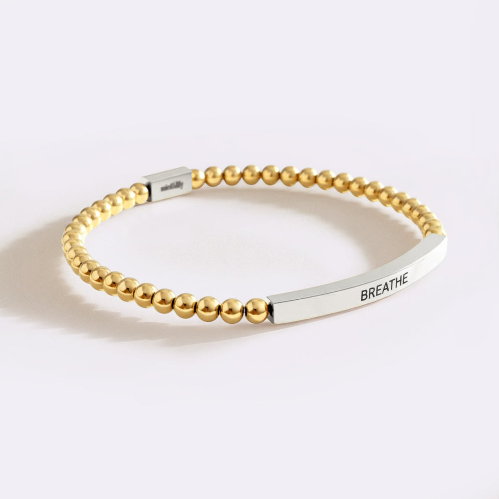 Gold beaded bracelet with a silver tag on a white background