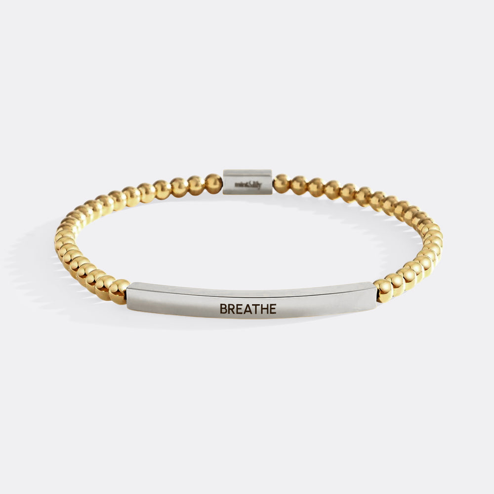 Gold beaded bracelet with silver bar and 'BREATHE' engraving on a white background