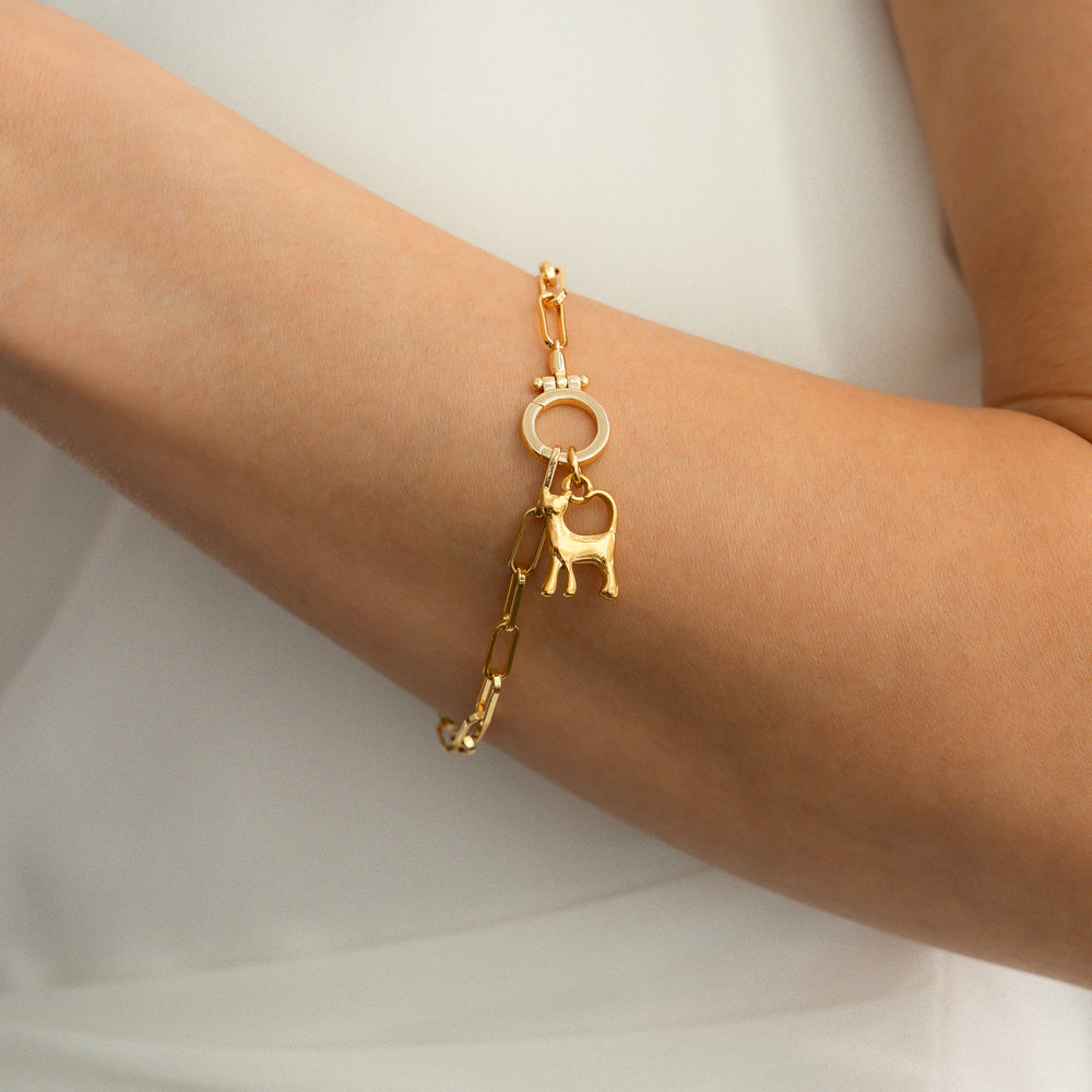 Gold bracelet with a cat charm on a person's wrist against a white background