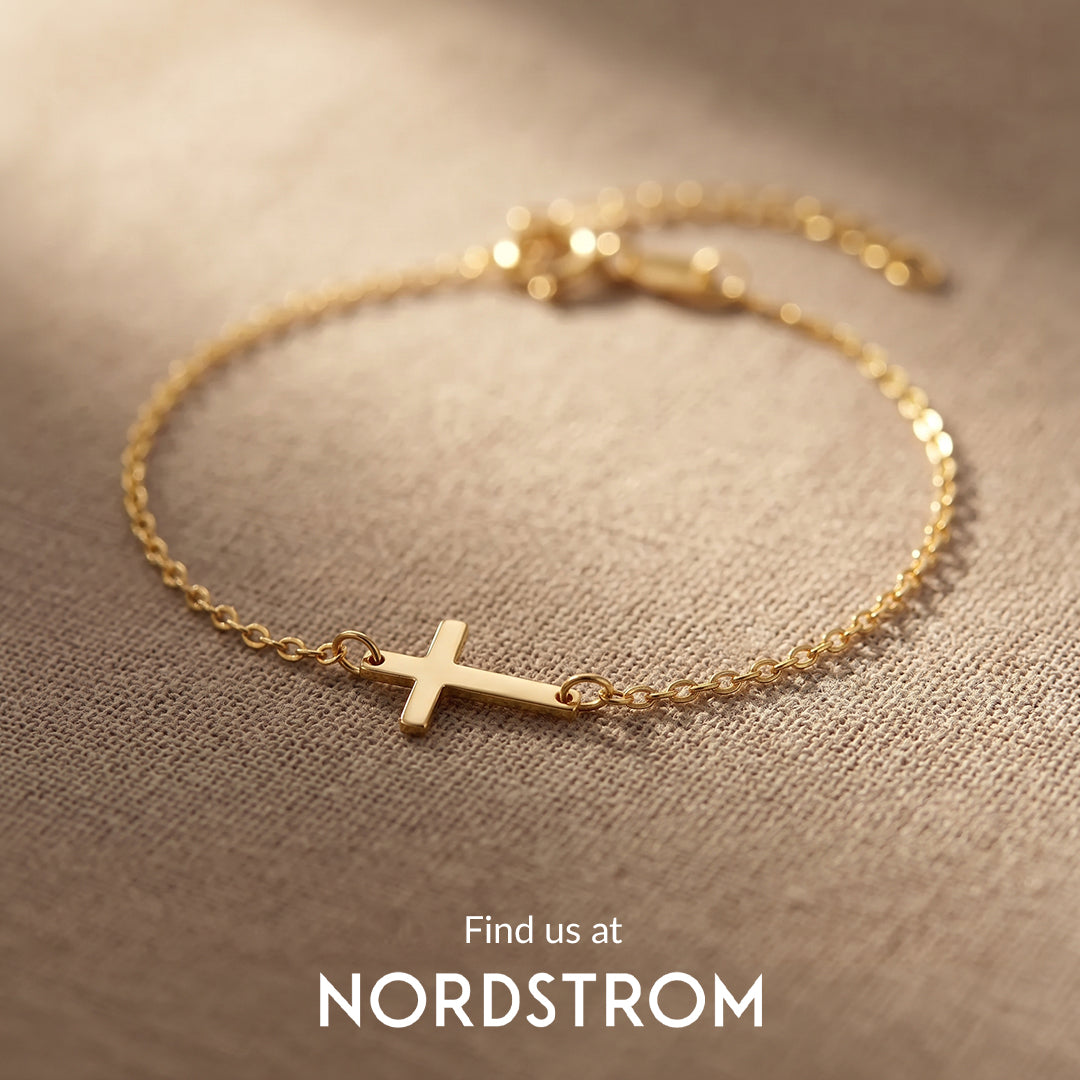 Gold bracelet with a cross charm on a beige fabric background, Nordstrom branding visible.