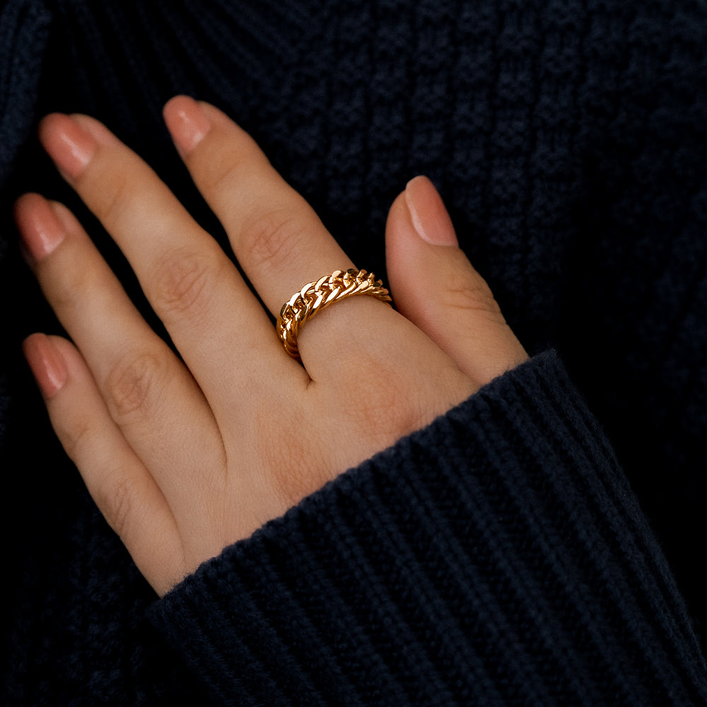 Close-up of a hand wearing a silver chain ring on a neutral background