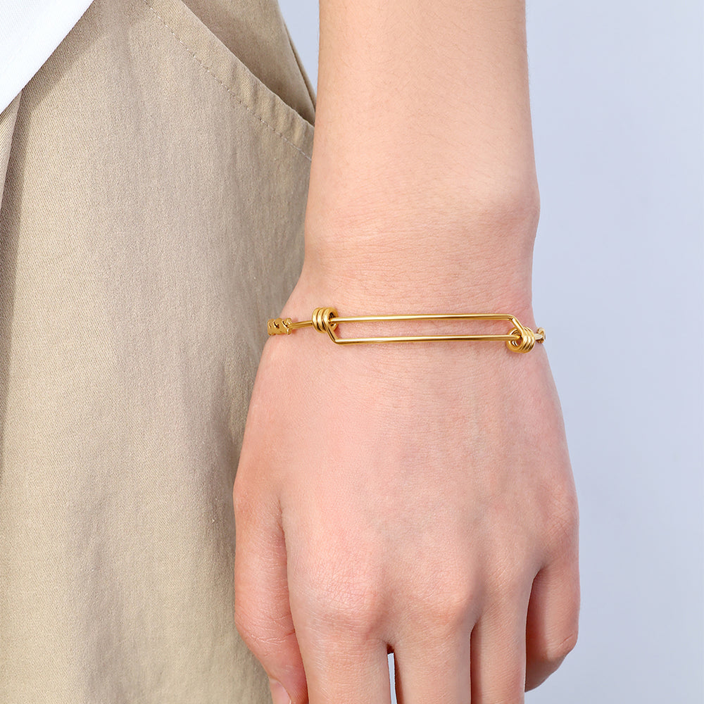 Gold bracelet on a wrist with a plain background