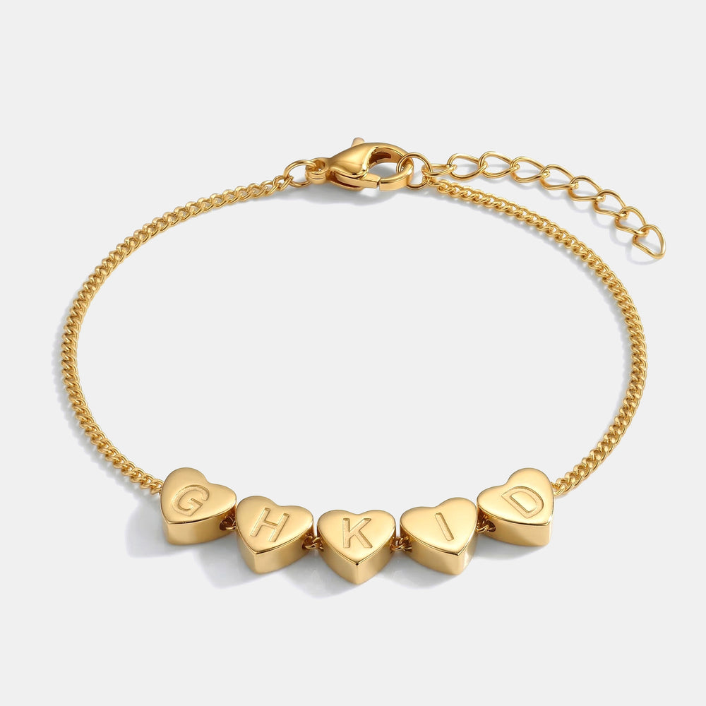 Gold bracelet with heart-shaped beads displaying letters on a white background