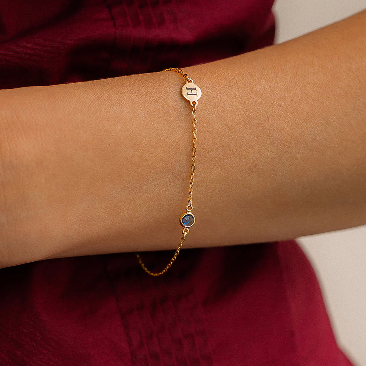 Gold bracelet with a blue gemstone on a wrist against a red fabric background