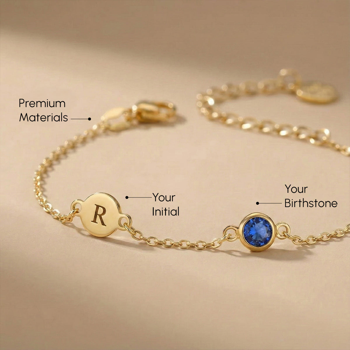 Gold bracelet with a blue gemstone and letter 'R' on a beige background