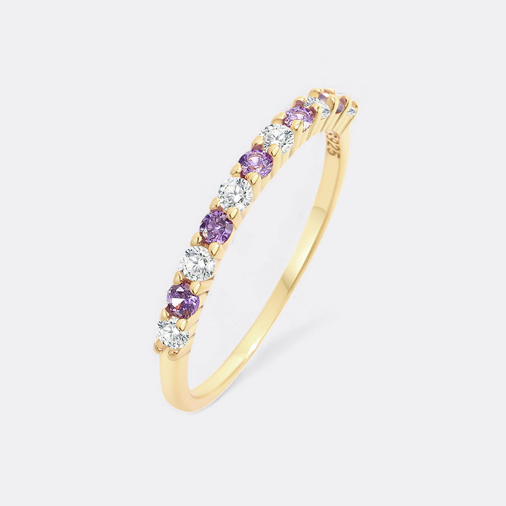 Gold ring with purple and clear gemstones on a light gray background