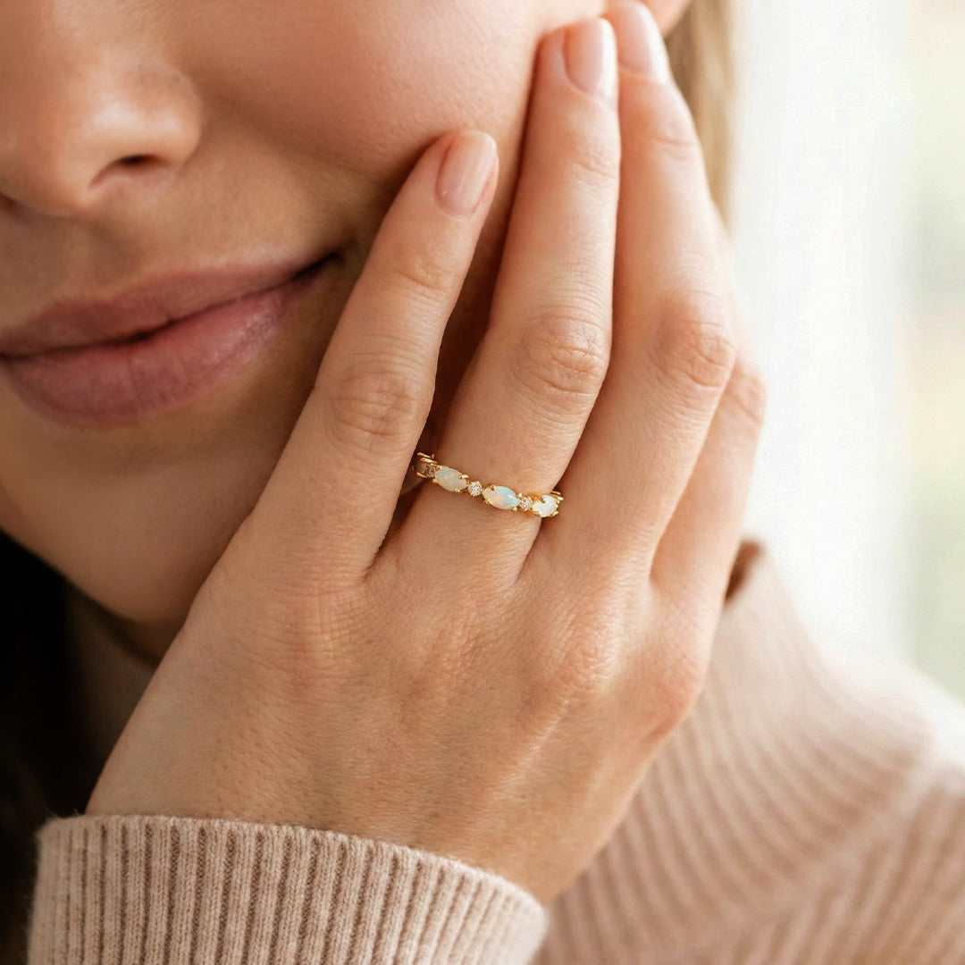 Close-up of a woman's hand wearing a gold ring with a diamond, touching her face.