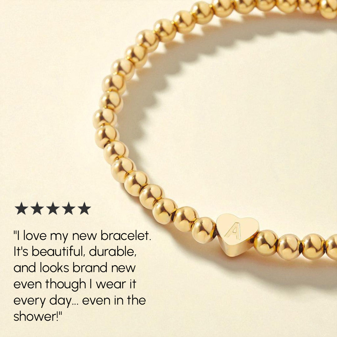 Gold beaded bracelet with heart-shaped charm on a beige background