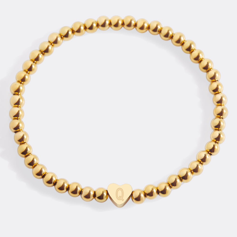 Gold beaded bracelet with a heart-shaped charm on a white background