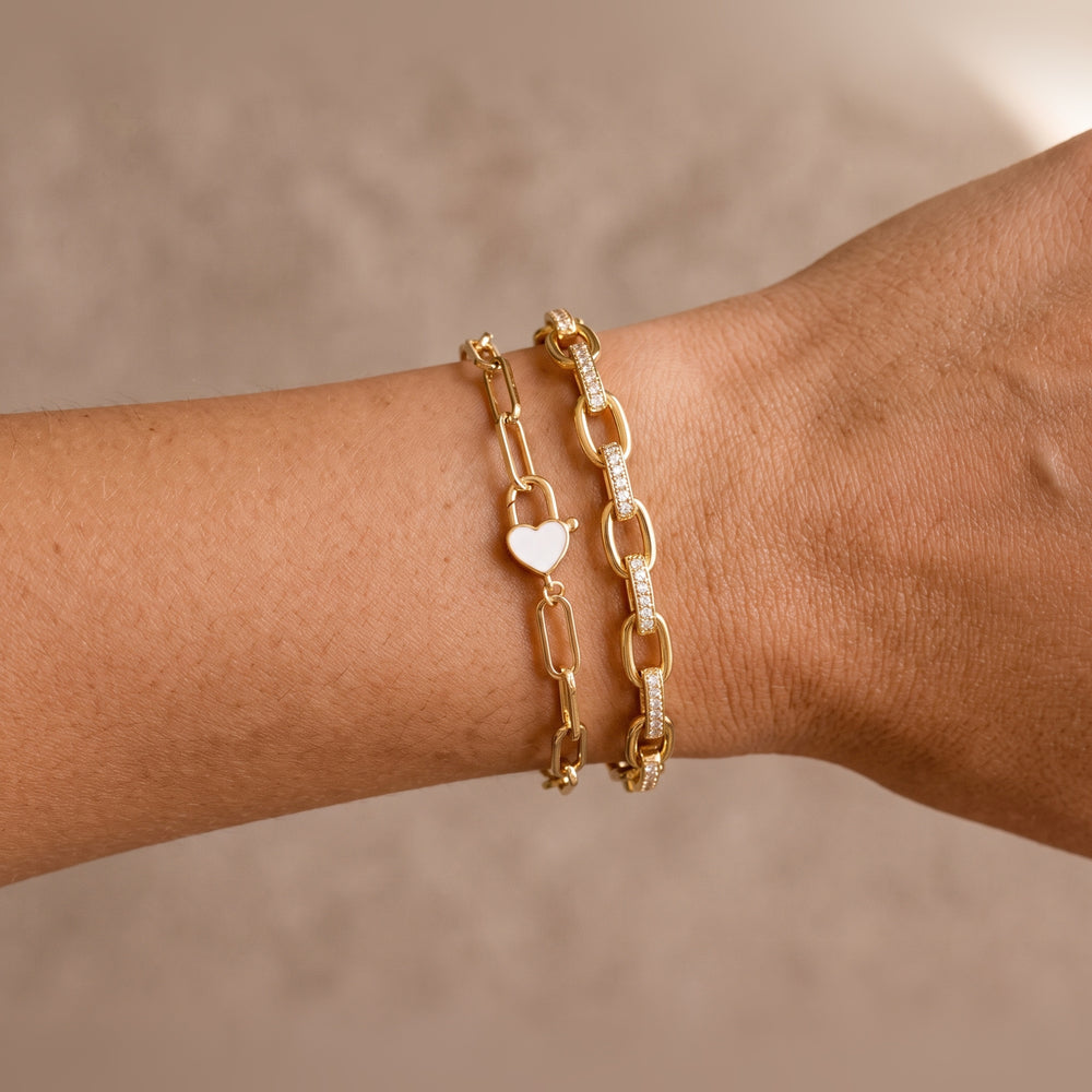 Model's wrist wearing the gold Heart Padlock Bracelet stacked with the Interlinked Diamond Paperclip Bracelet