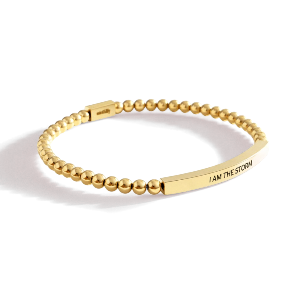 Gold beaded bracelet with a bar section displaying 'I AM THE STORM' on a white background