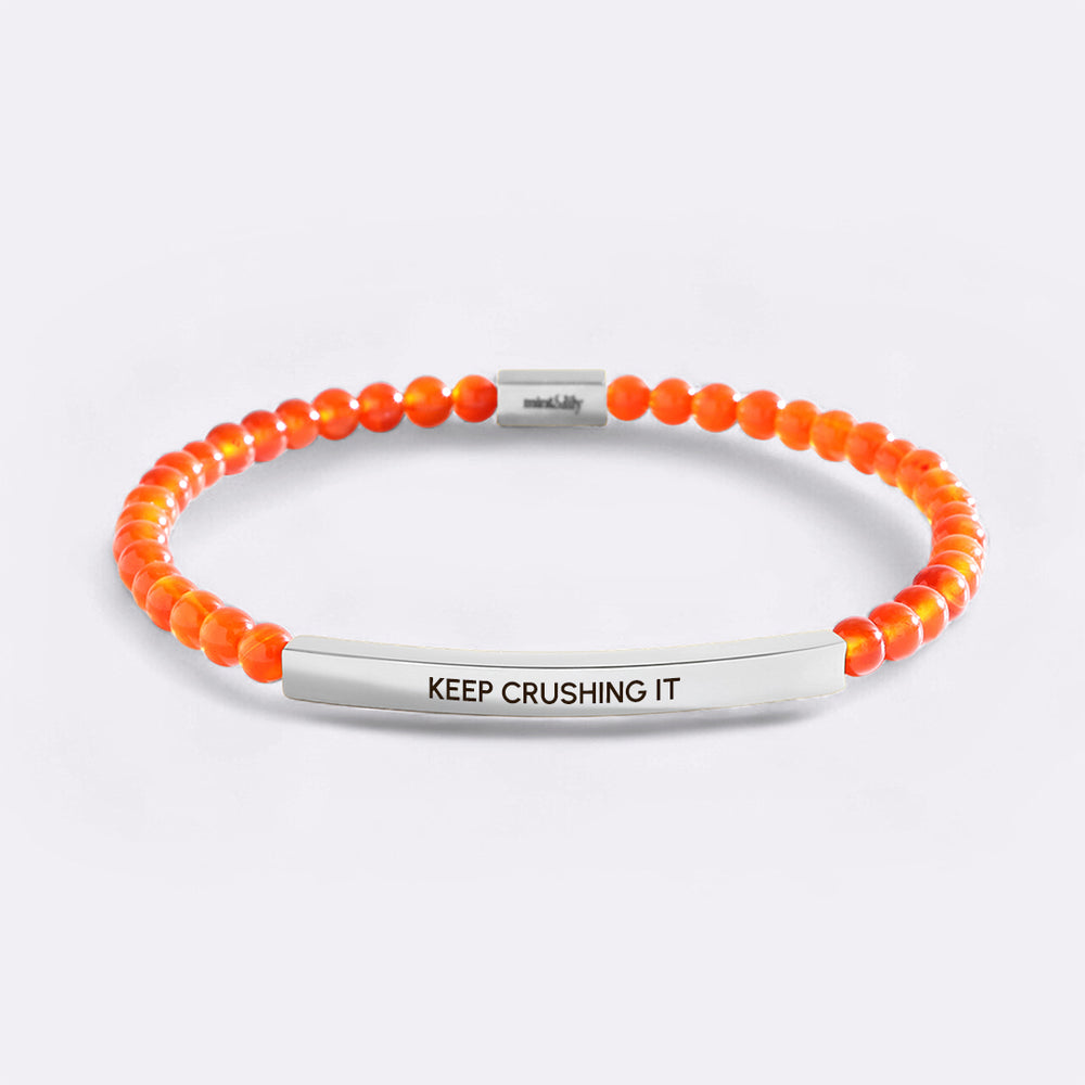 Orange beaded bracelet with silver bar and 'KEEP CRUSHING IT' engraving on a light gray background