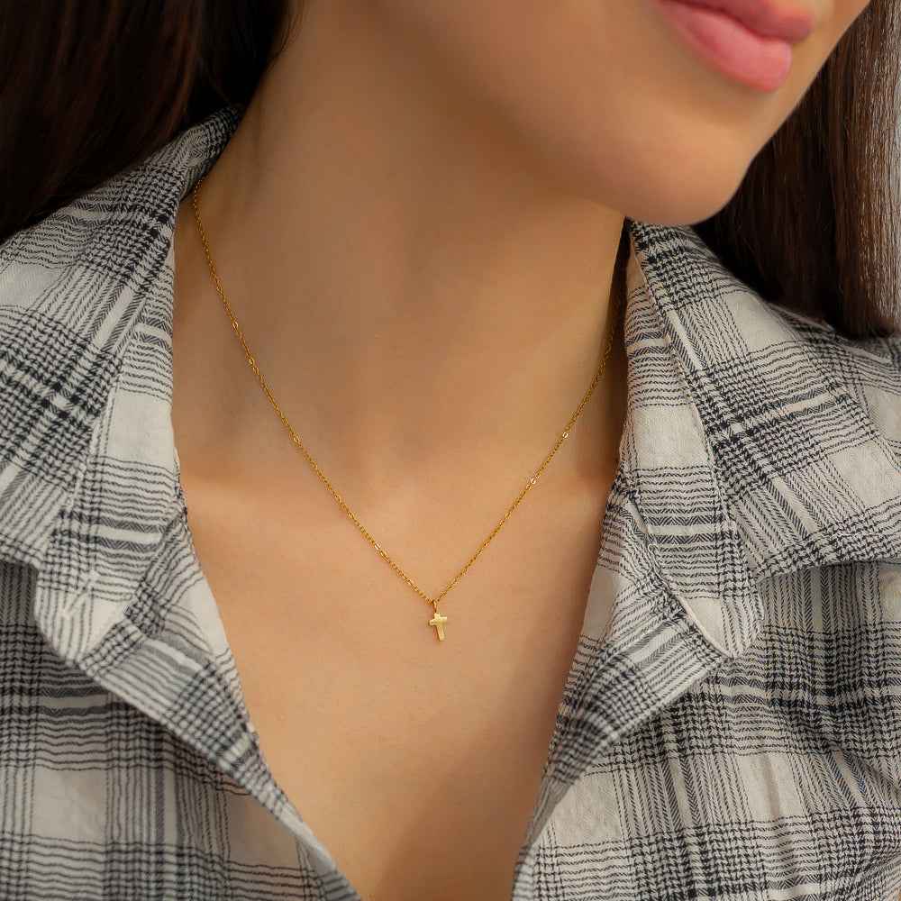 Gold necklace with a small pendant worn by a person in a plaid shirt.