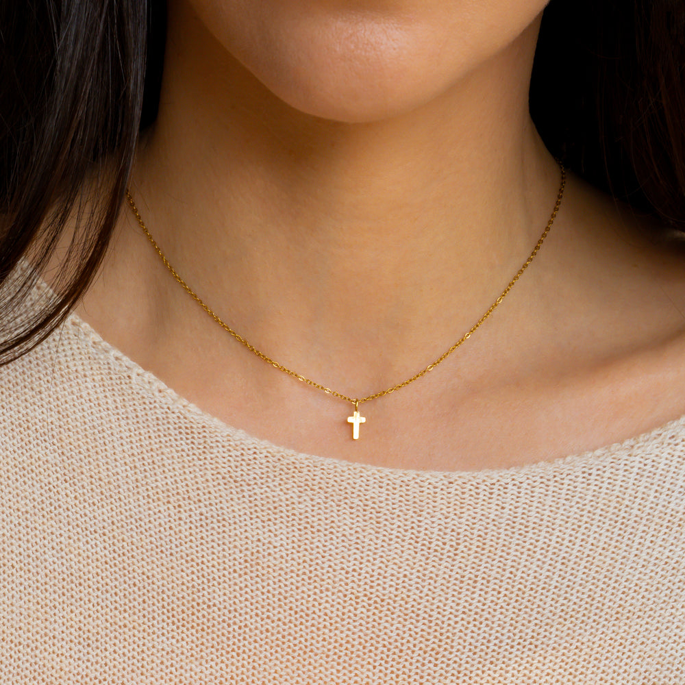 Gold necklace with a cross pendant worn by a person against a neutral background