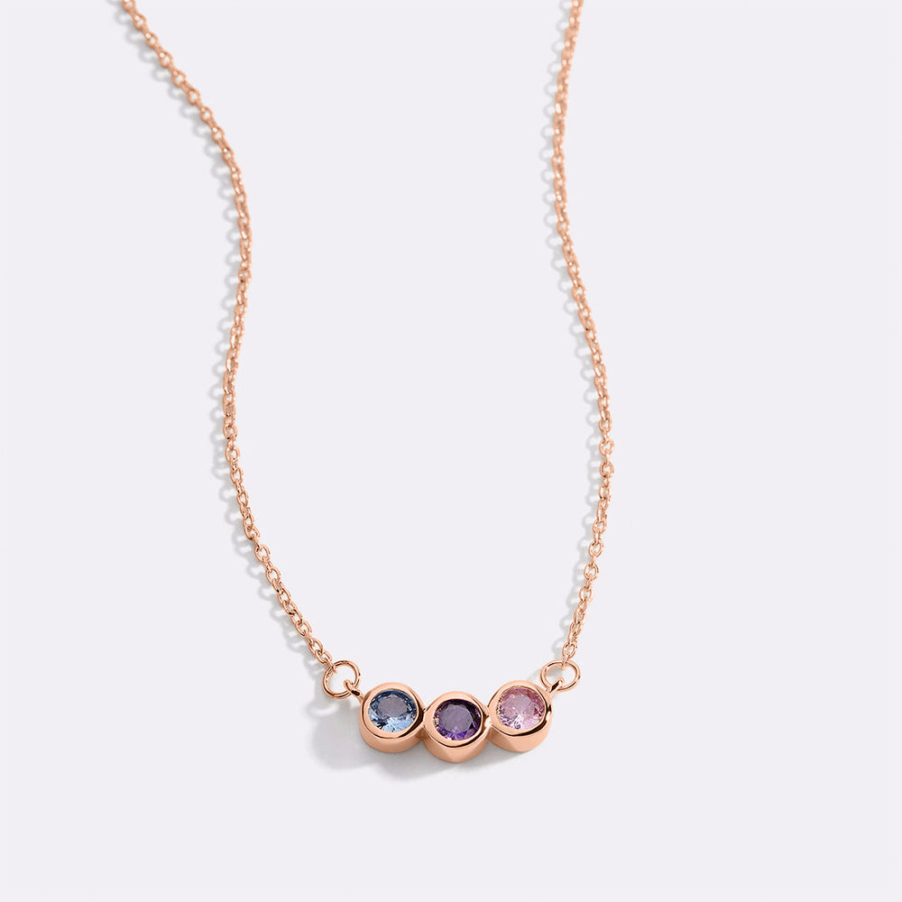 A dainty gold-colored necklace featuring a series of round charms with multicolored birthstones on a black background.