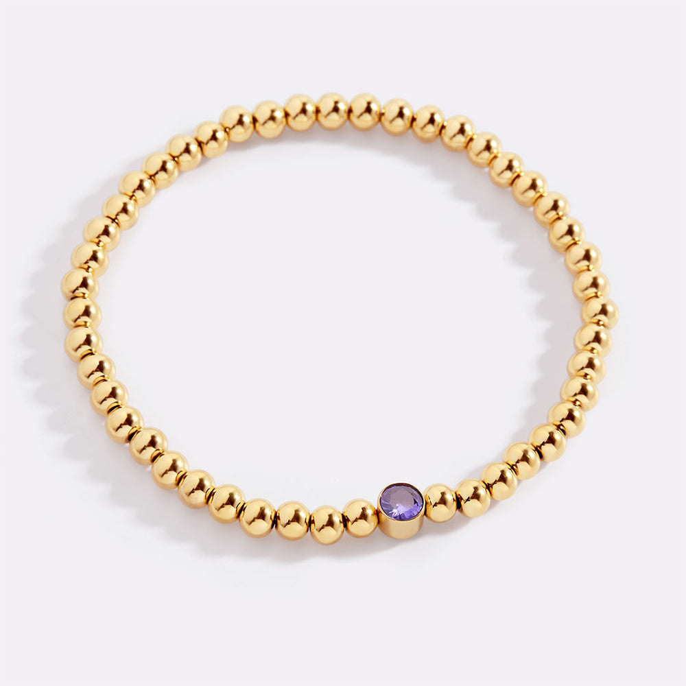 Gold beaded bracelet with a purple bead on a white background