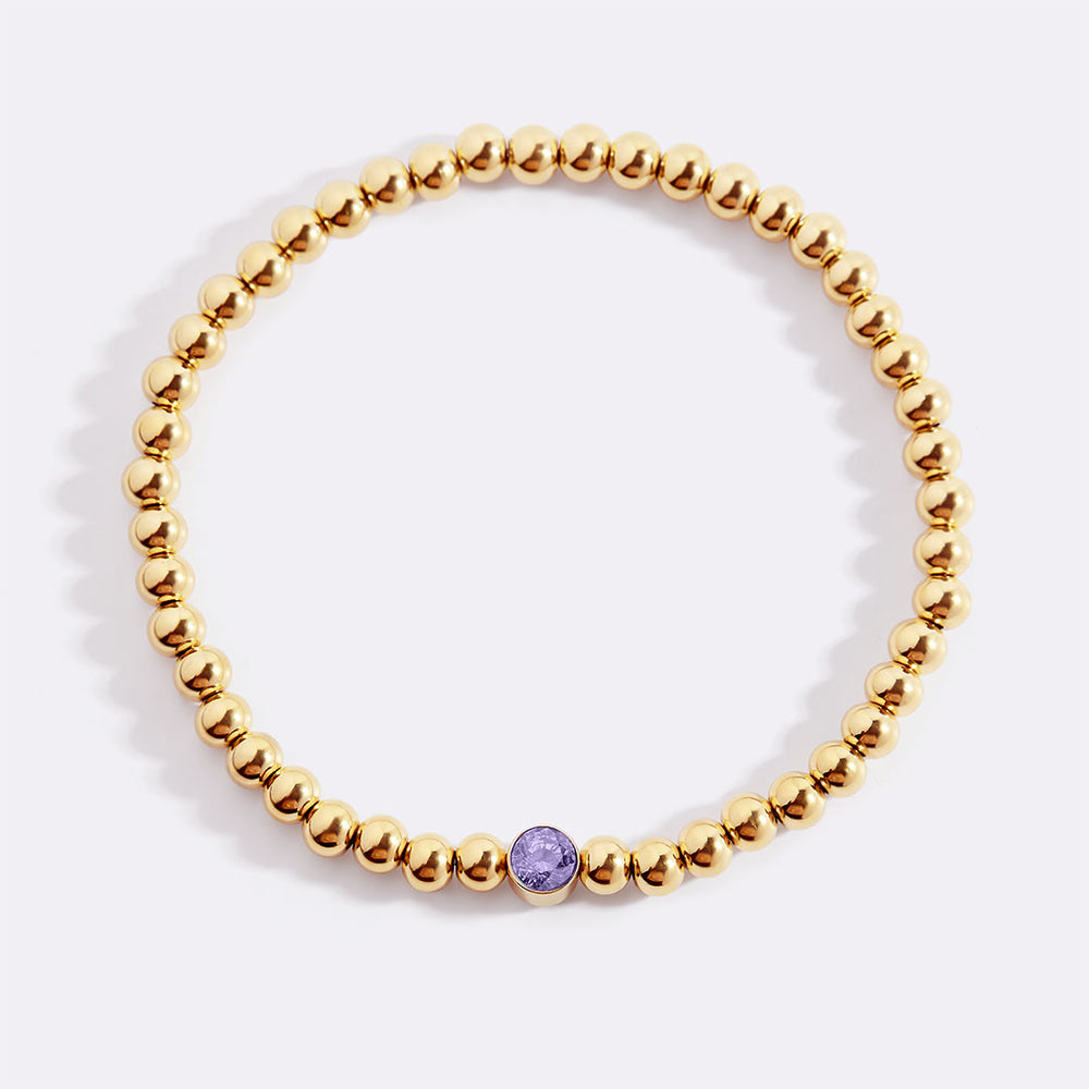 A gold-colored beaded bubble bracelet with a central birthstone charm, displayed against a black background.