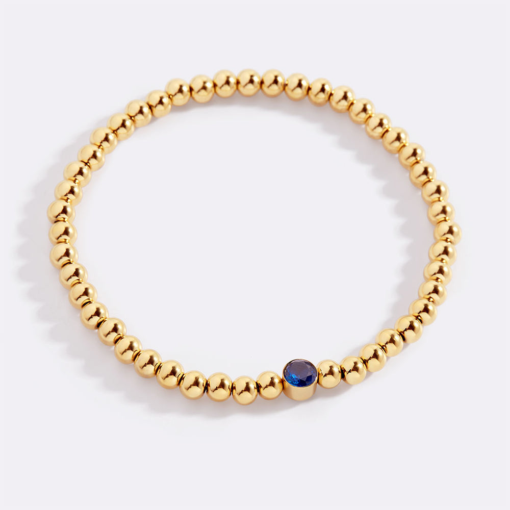 Gold beaded bracelet with a blue gemstone on a white background