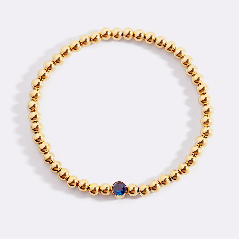 Gold beaded bracelet with a blue stone on a white background