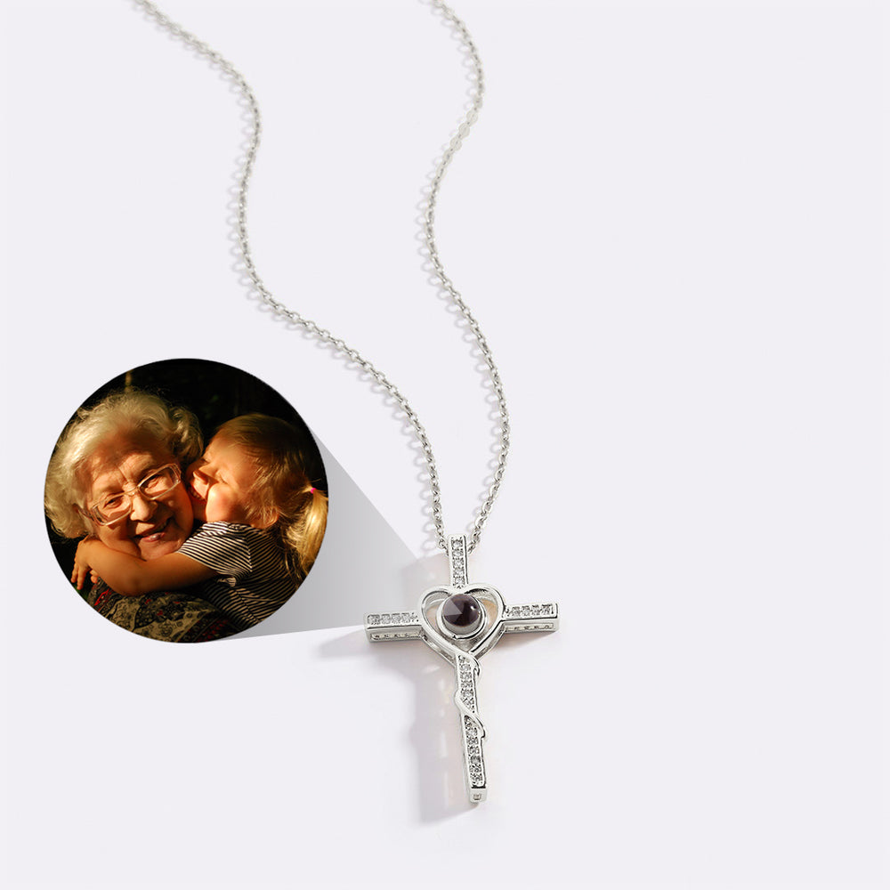 An 18k gold photo necklace with a heart and cross pendant, displayed alongside an inset image of an older couple smiling.