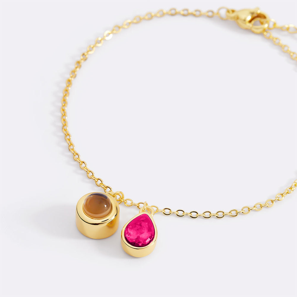 Gold bracelet with two gemstone charms on a white background
