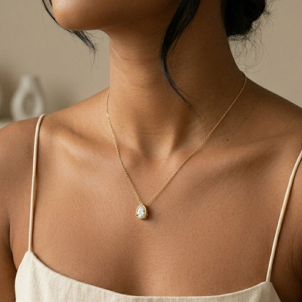 Gold necklace with a teardrop-shaped pendant on a person wearing white tank top.
