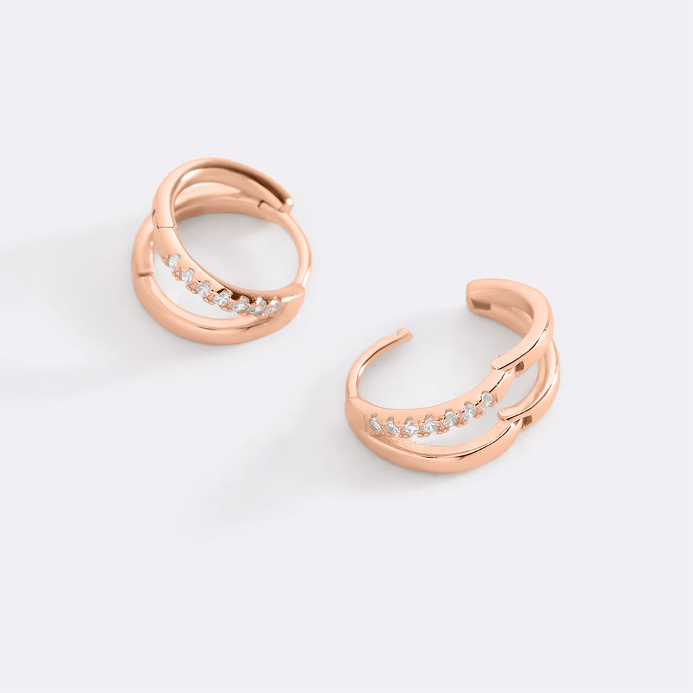 Rose gold hoop earrings with embedded diamonds on a light gray background