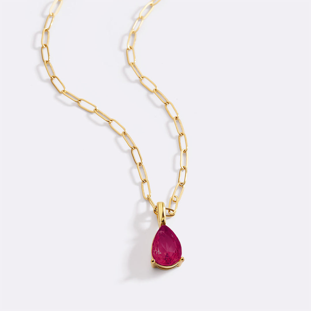 Gold necklace with a teardrop-shaped ruby pendant on a white background