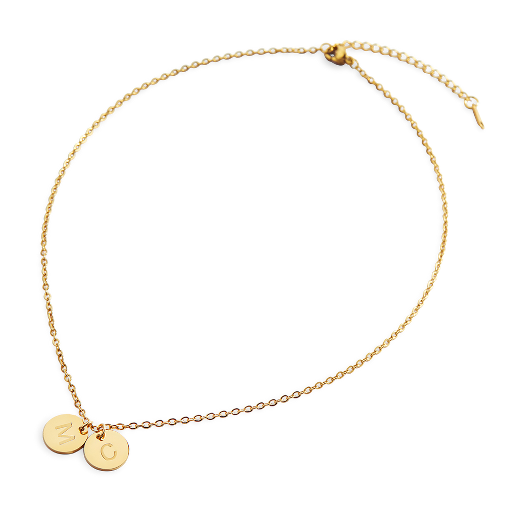 A gold-colored dainty disc initial necklace with two pendant discs personalized with the initials 'MC'.