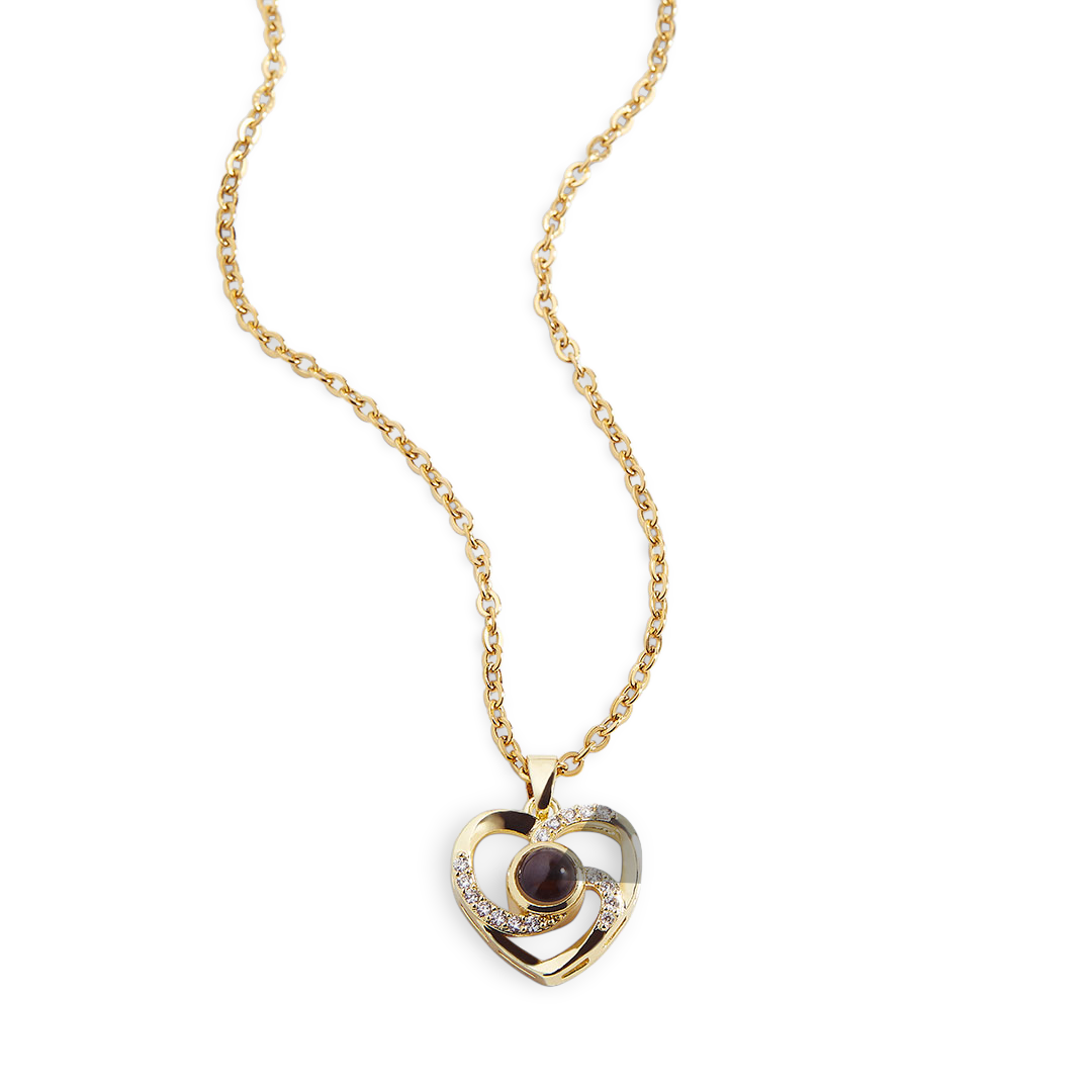 A gold-tone heart-shaped necklace with a pave setting featuring a photo projection stone at the center, displayed alongside an inset image of a woman holding a baby.