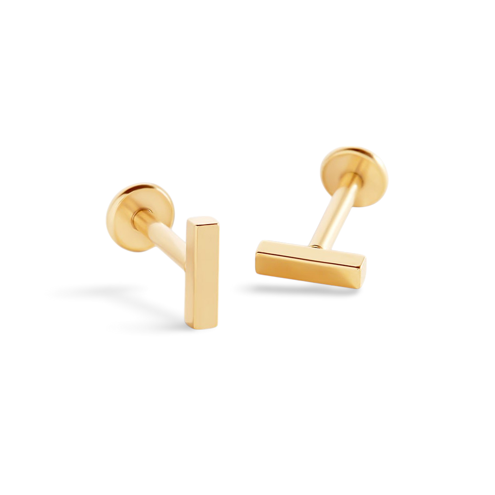 A pair of flatback sleeper earrings with a gold-colored bar pendant attached to a black backing, set against a black background.