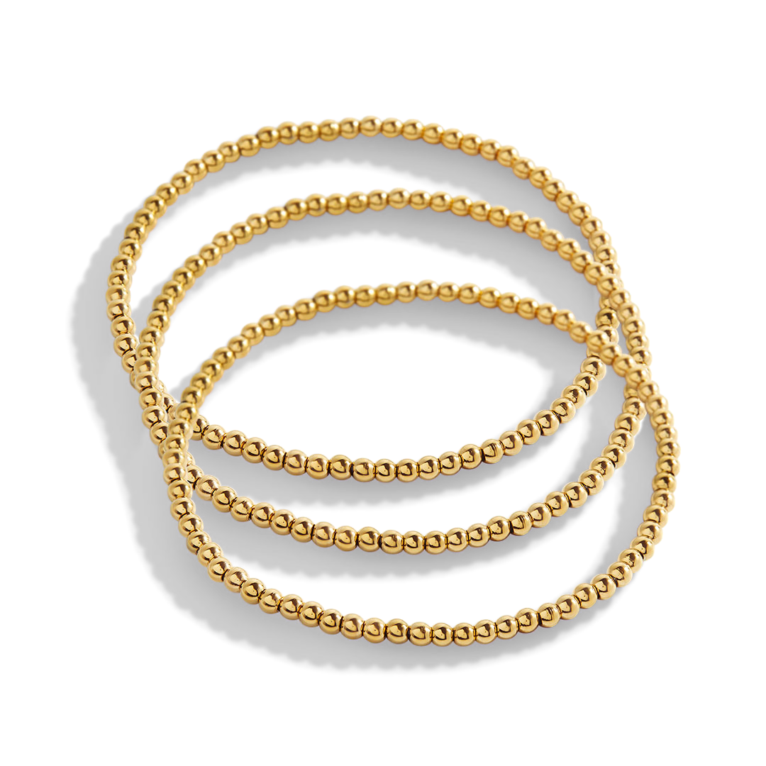 Set of three gold beaded bracelets on a light gray background