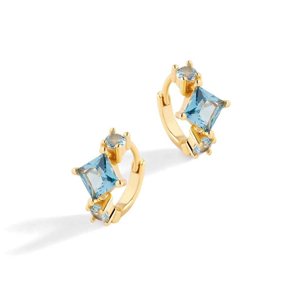 Gold hoop earrings with blue gemstones on a light gray background