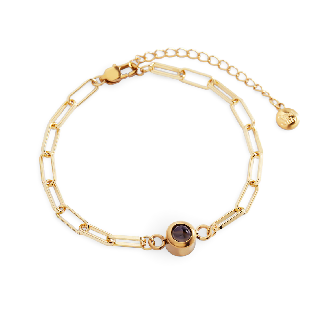 Gold chain bracelet with a purple gemstone on a white background