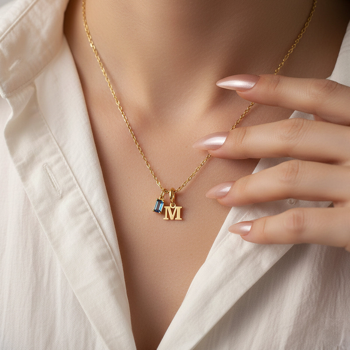 Gold necklace with a 'M' pendant worn by a person in a light-colored shirt.