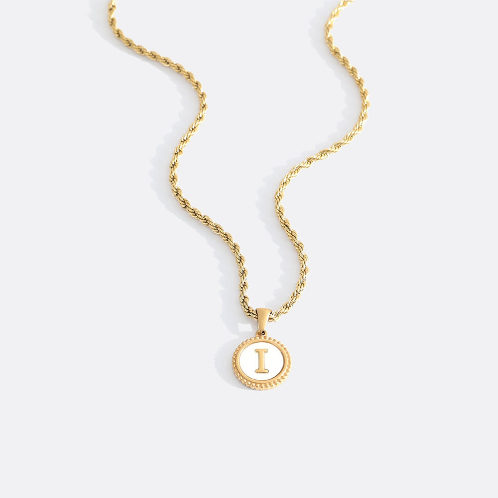 A gold rope chain necklace with a mother of pearl disc pendant engraved with a letter.