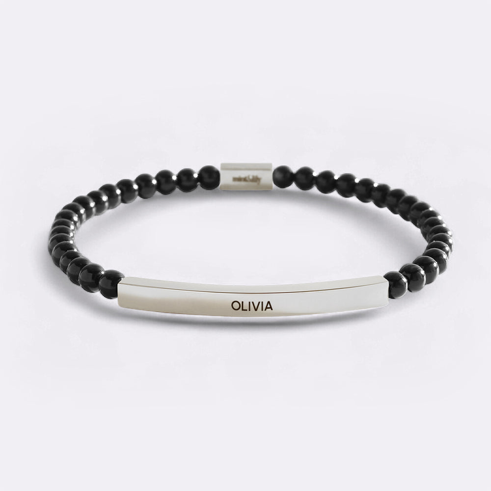 Black beaded bracelet with a silver nameplate on a light gray background