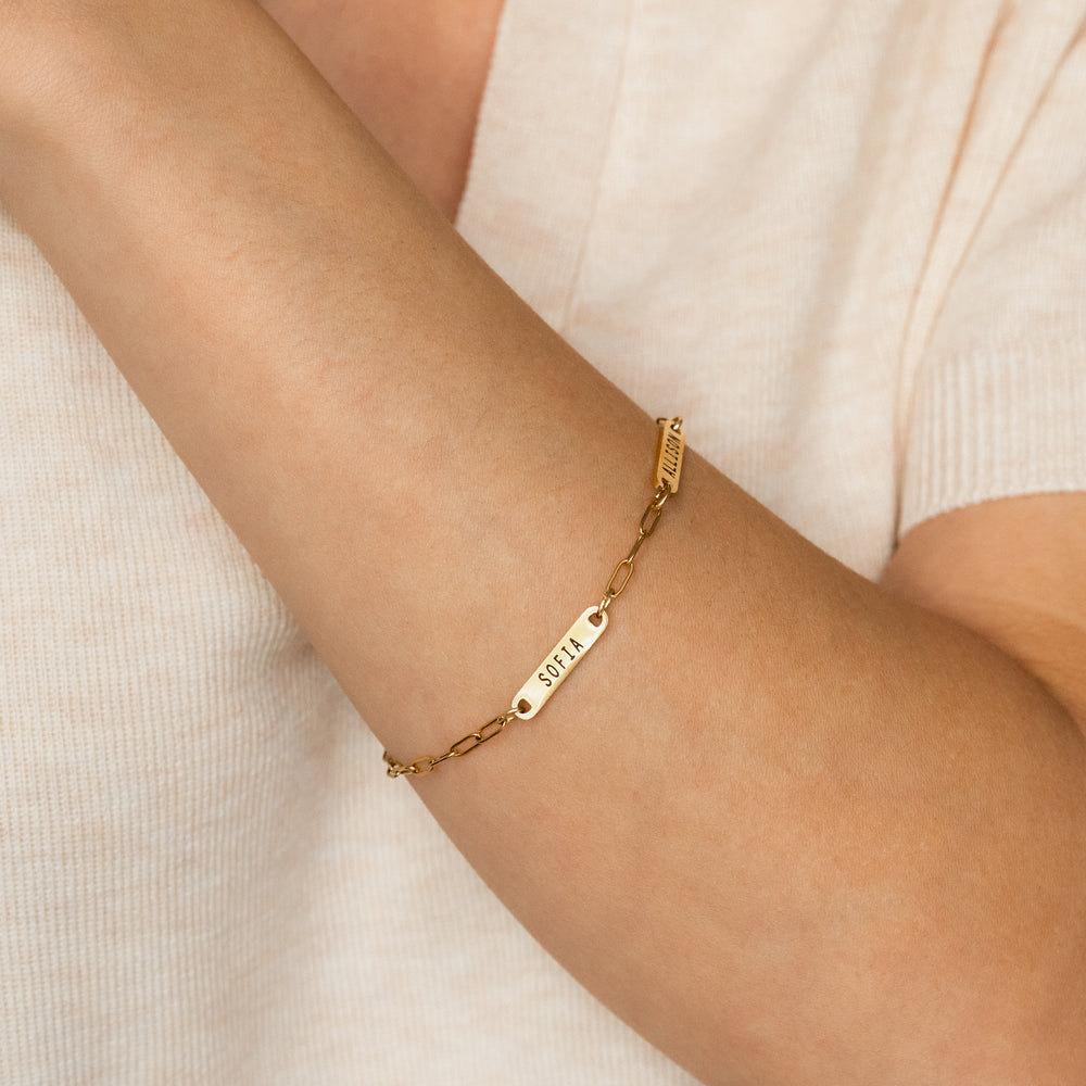 Gold bracelet with engraved name on a person's wrist against a neutral background